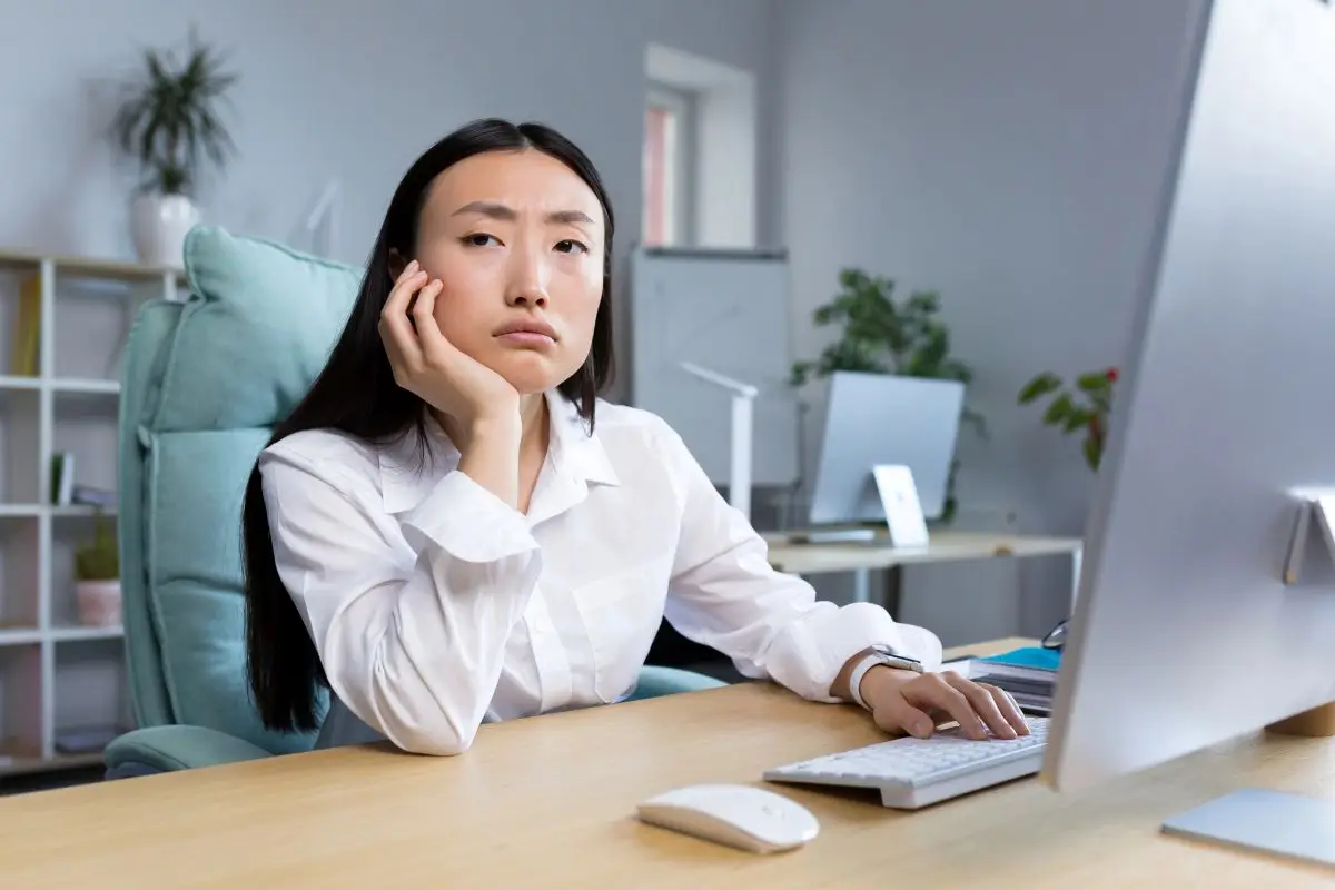 A Singaporean SME owner looking bored while reviewing financial records at her desk.